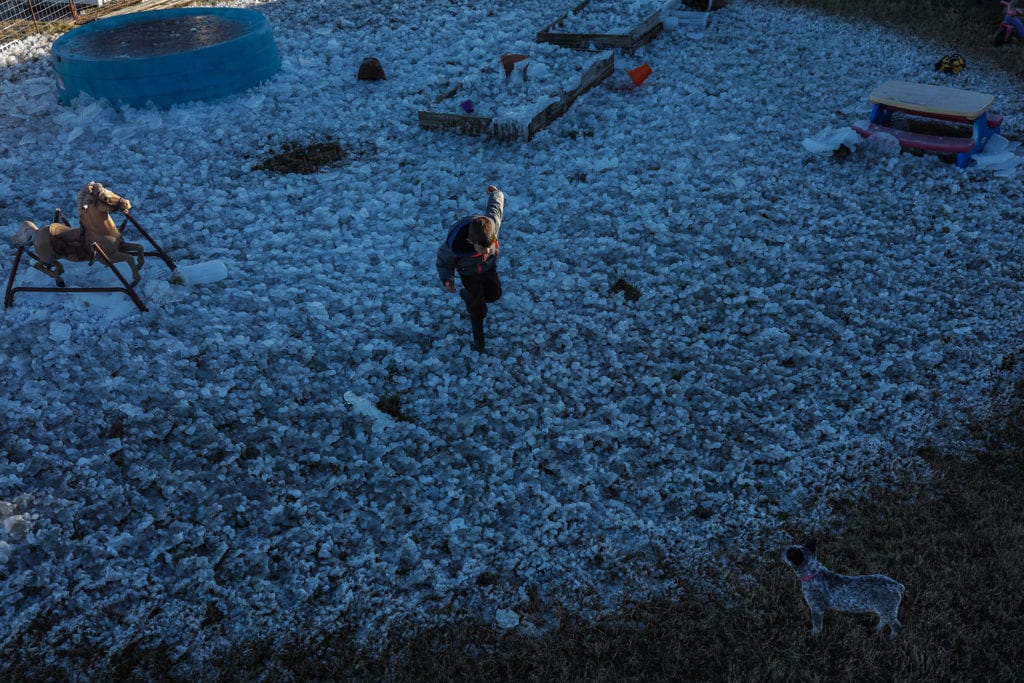 boy runs across field of ice with arm in sunshine