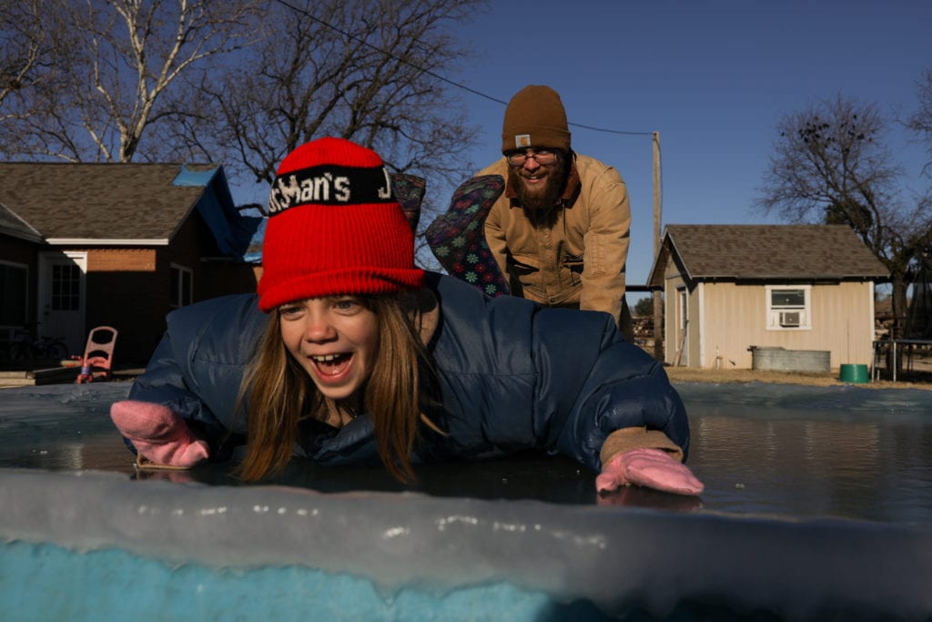 girls slides across ice while dad pushes her