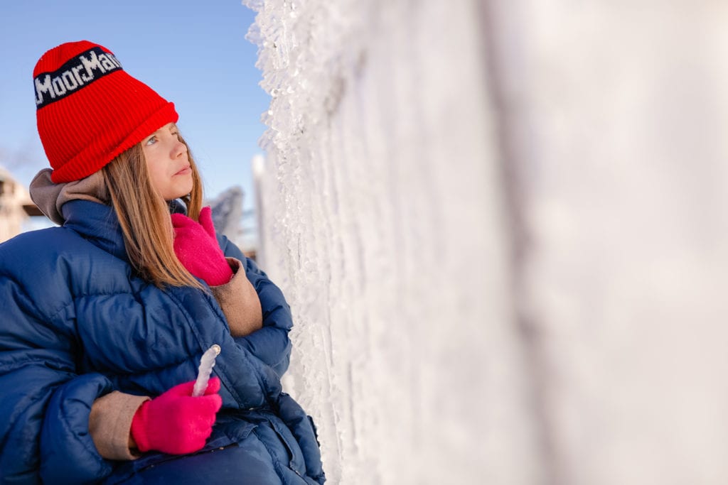 girls looks up at ice wall while holding icicle