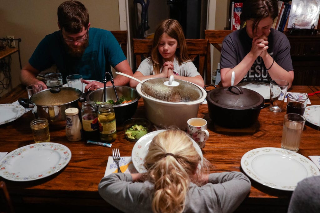 family prays while girl presses plate against face