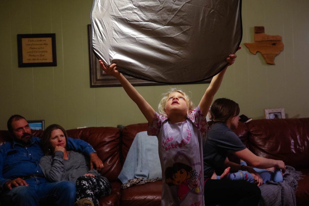 girl holds windscreen reflector up to light as family look on