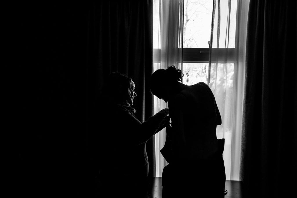 bride helps bridesmaid into dress