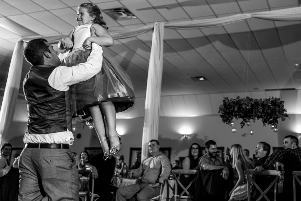 Groom holds daughter up in the air during first dance together