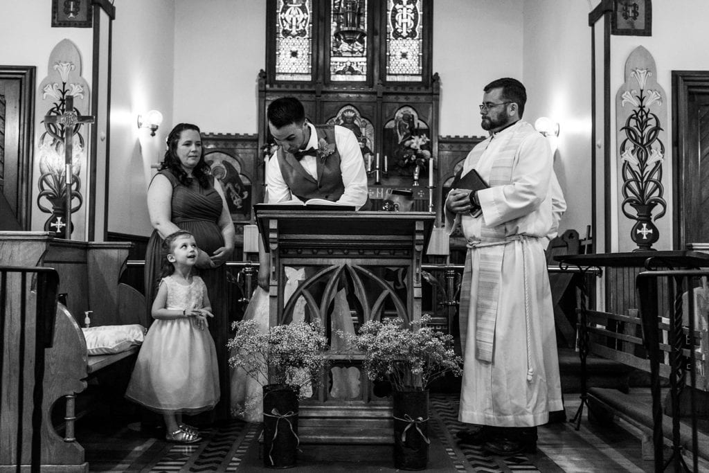 flower girl looks up at groom as he signs wedding register
