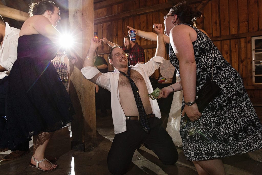 Man dances with shirt open while women prepare to hand him money at Williamstown Fairgrounds wedding reception