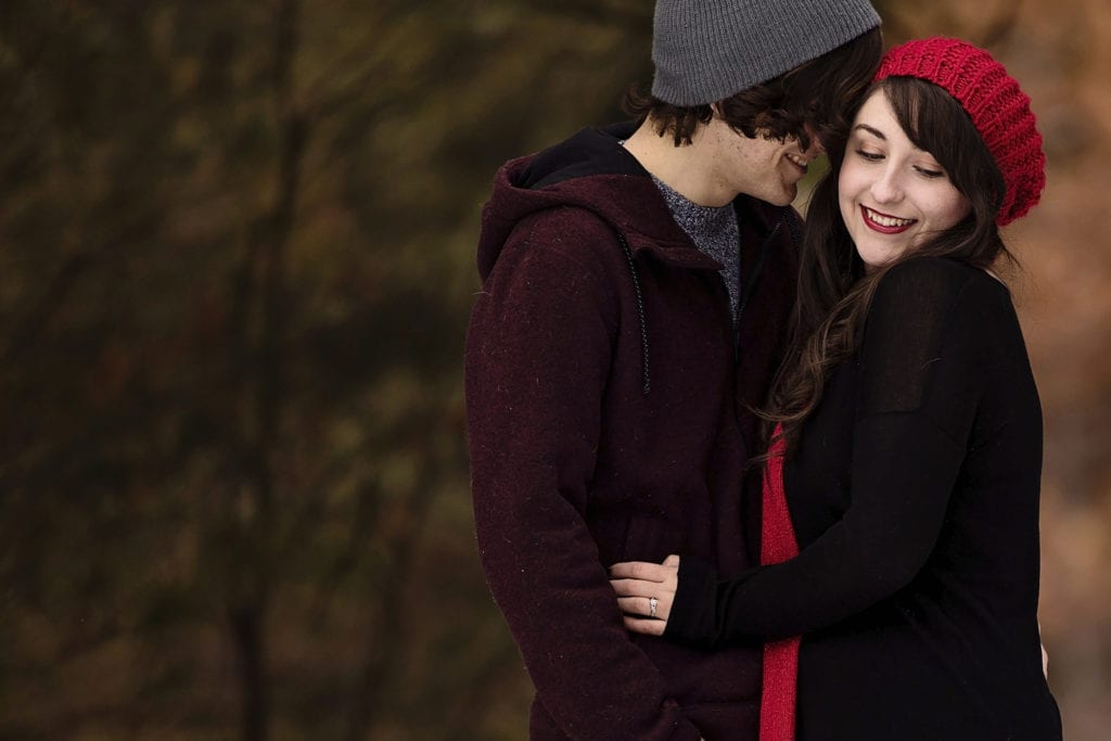 girl in red scarf and tuque being nuzzled during cozy winter engagement session