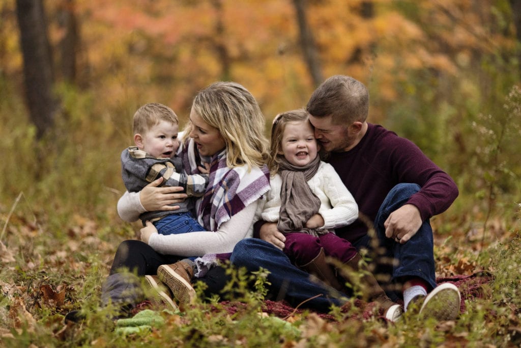 family sits on grass as mom plays with son and dad plays with daughter