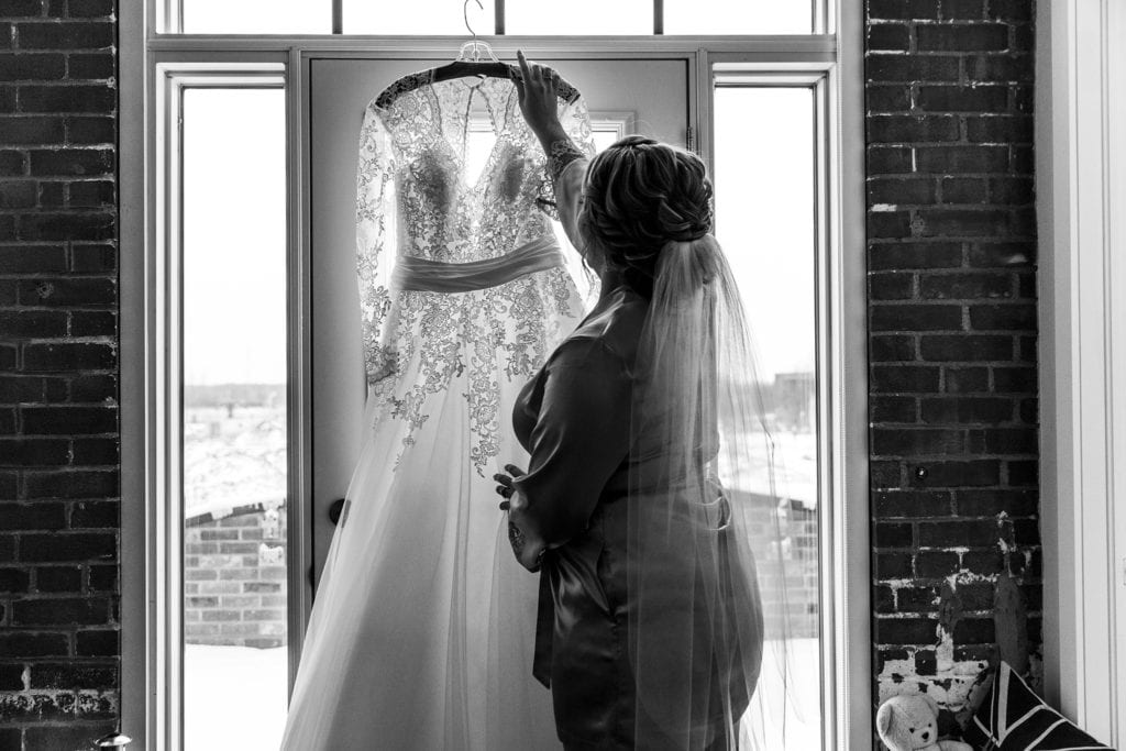 bride removes dress from doorway while wearing a dressing gown