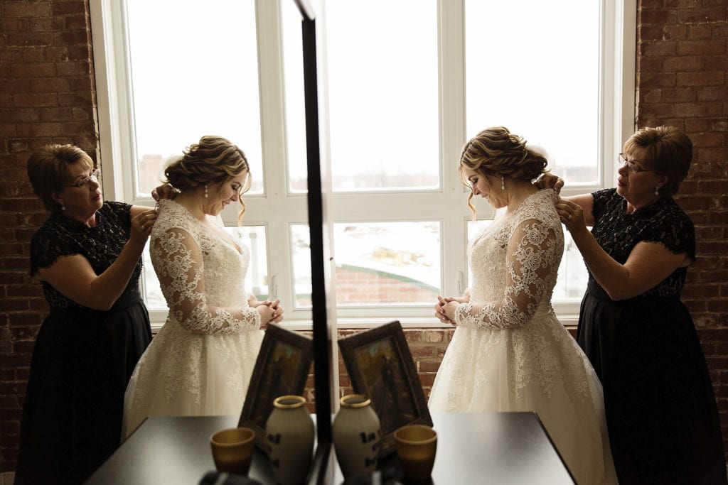 mirror image of mother of the bride helping to fasten bride's dress