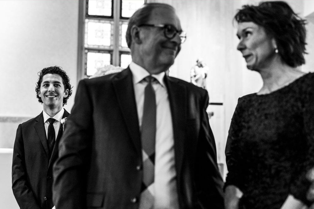 parents of the groom smile at each other while groom watches bride make entrance for Cornwall wedding ceremony