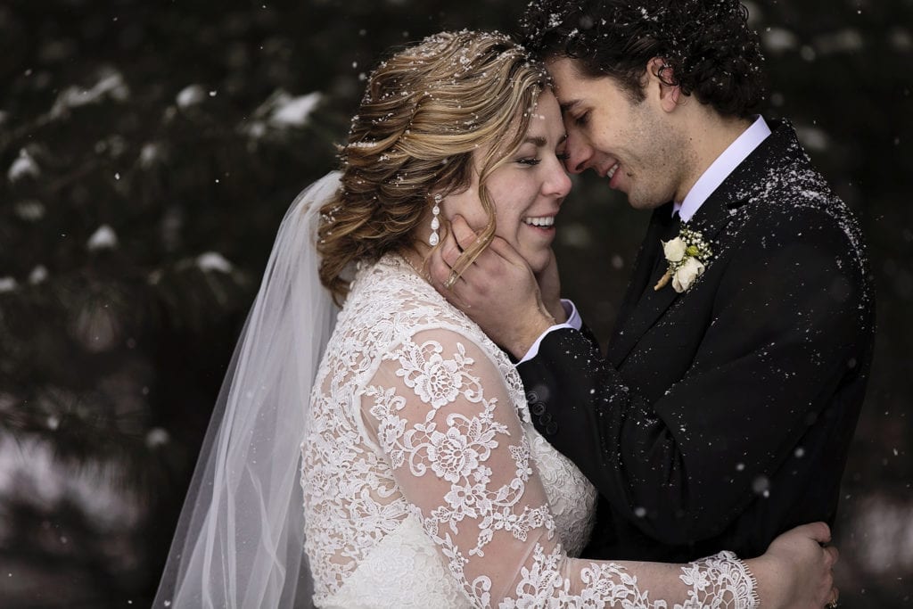 groom holds bride close during snowy Cornwall winter wedding portraits