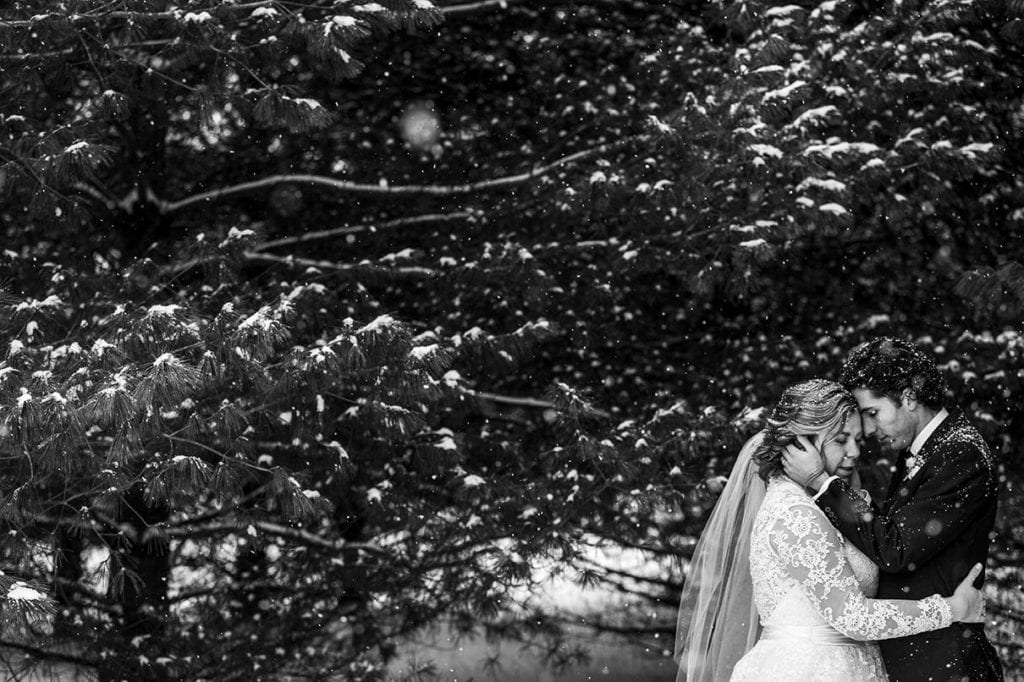 groom cuddles close to bride while touching her face during snowy Cornwall winter wedding portraits