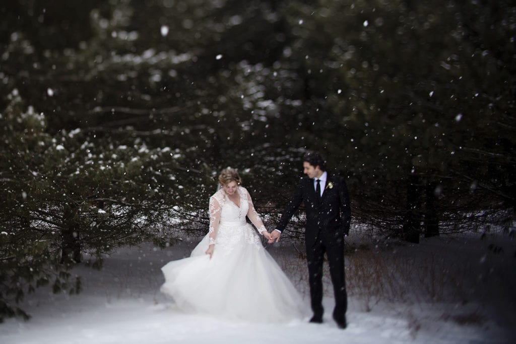 bride swishes dress in front of pine trees during snowy Cornwall winter wedding