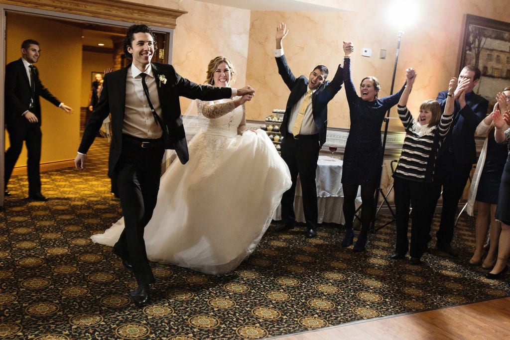 bride and groom hold hands while walking into room with cheering guests