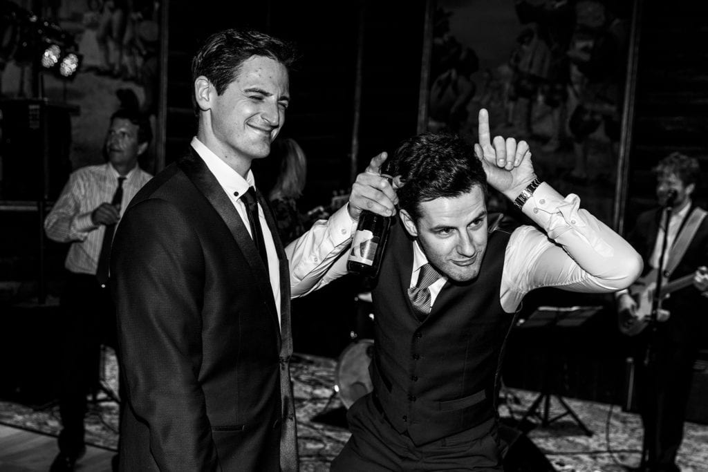 man with fingers pointing up from head like bull stands next to wincing groom