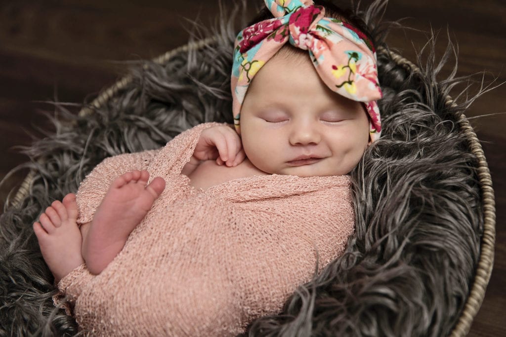 baby in floral headband and pink wrap smiles during Cornwall newborn photography session