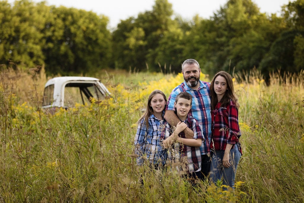 Dad standing in grassy field with three kids all in plaid