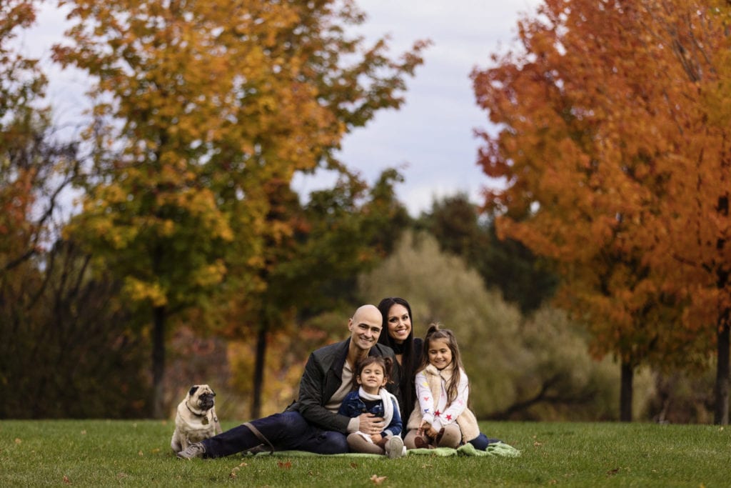 family on grass with girls in scarves and jackets and pug sitting beside dad