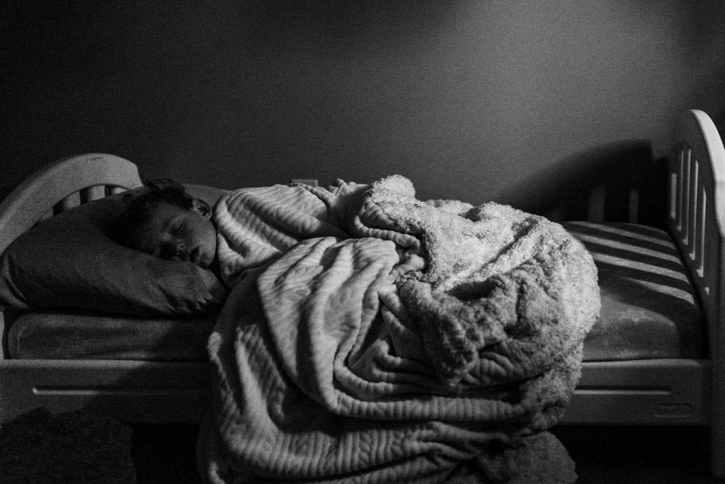 boy sleeps in small bed under furry blanket