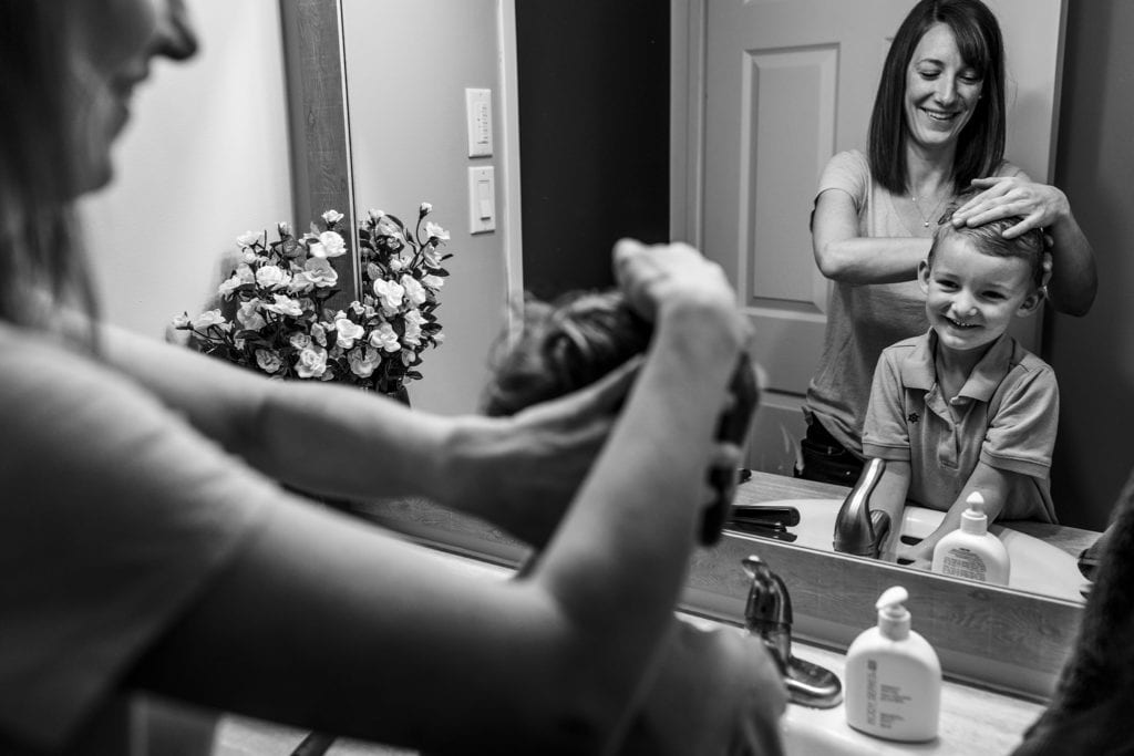 boy looks in mirror happily as mom styles his hair