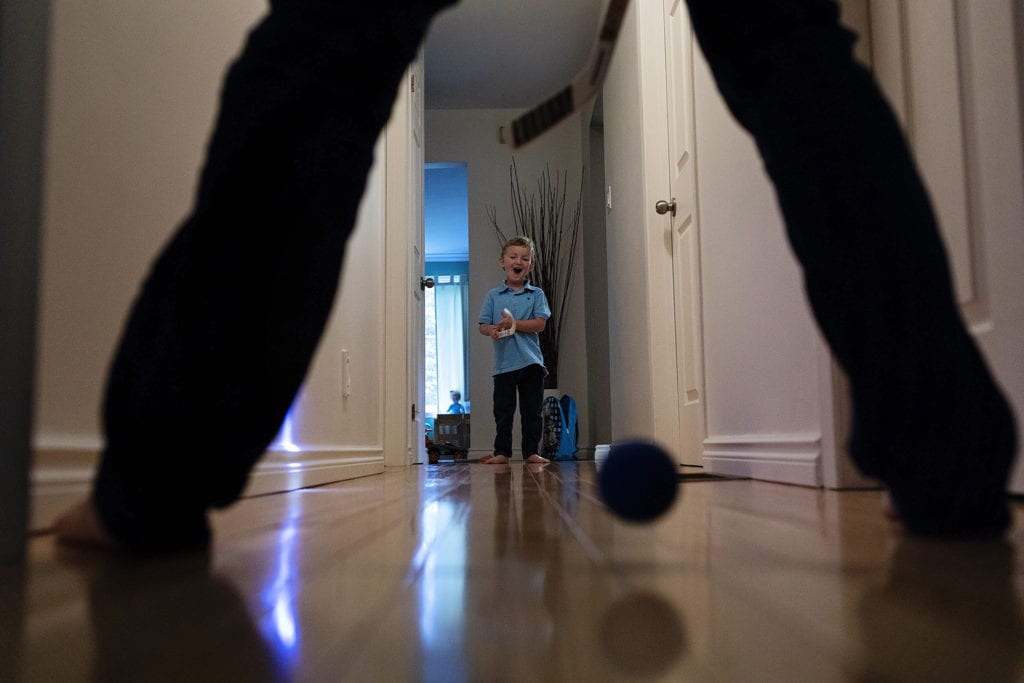 boy with hockey stick in hallway reacts happily as ball goes between father's legs