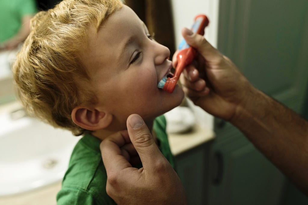 boy in green shirt gets help with toothbrush from dad