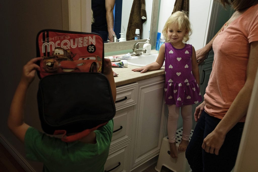 boy wears lunchbag on head while sister looks on from bathroom stool