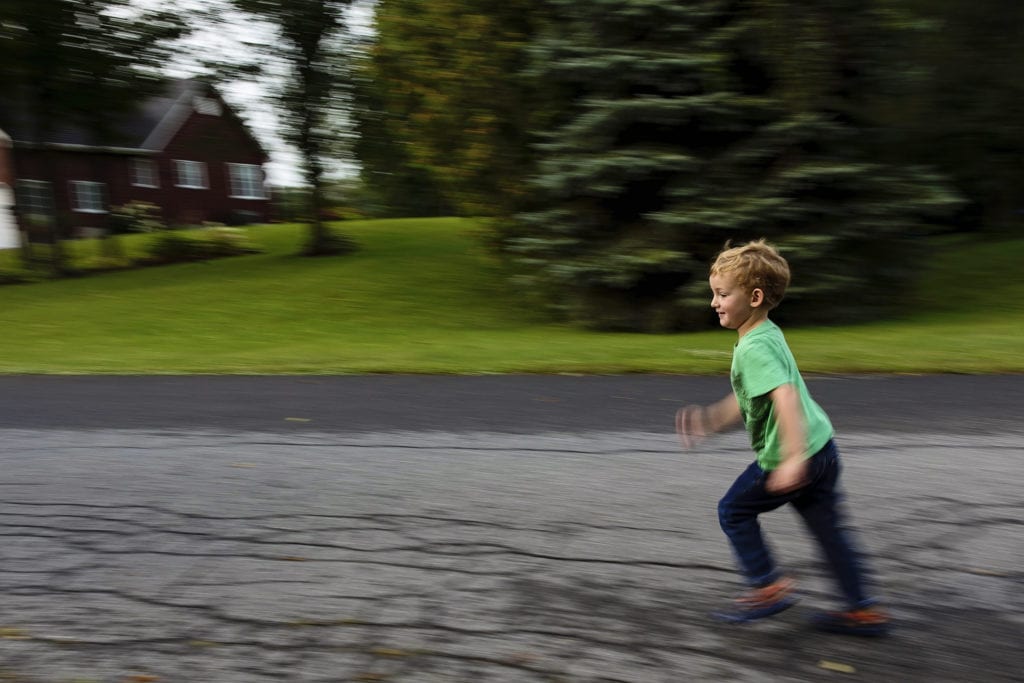 panning shot of boy running down street