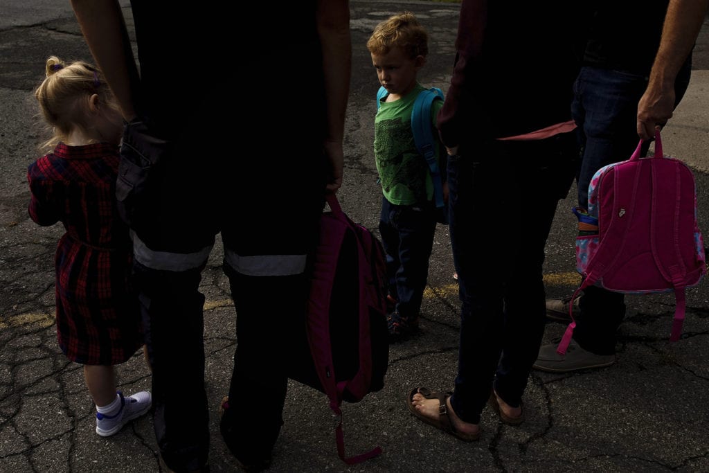 two children stand among adults holding backpacks