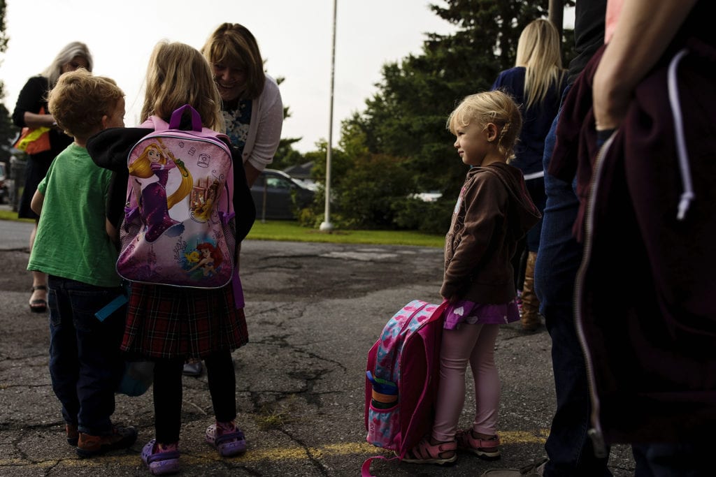 teacher bends to talk to two children while little girl looks on