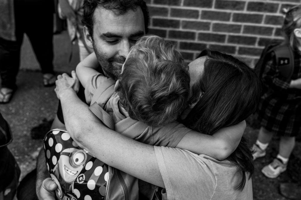 boy hugs mom and dad while wearing backpack