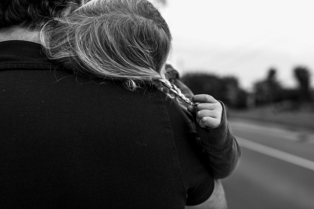 girl snuggles into dad's neck while playing with braid