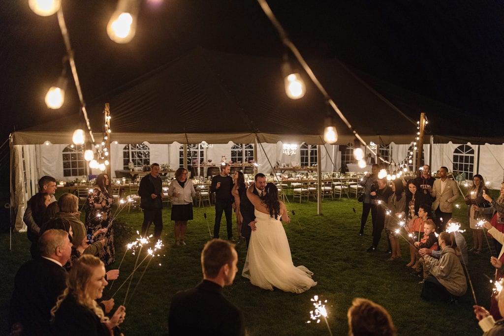 bride and groom have first dance under string lights while backyard wedding guests hold sparklers