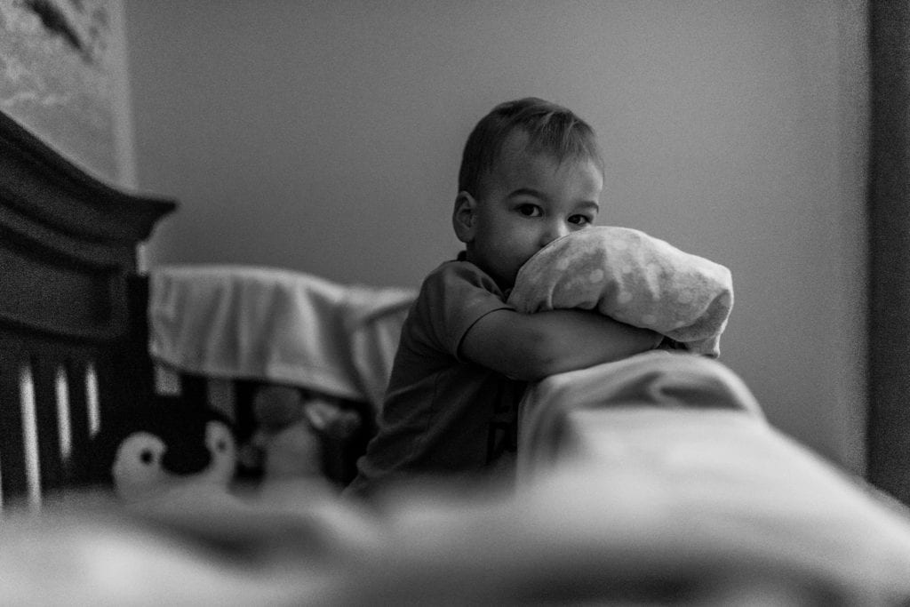 toddler stands in crib with blanket looking at camera