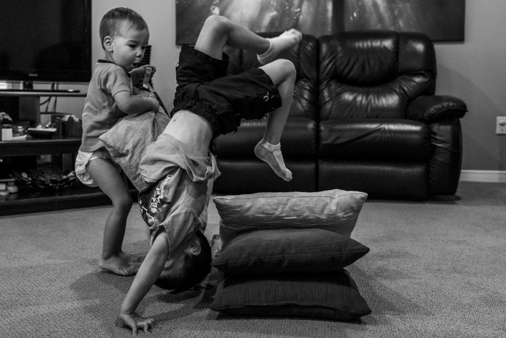 boy in handstand flips onto pillows while brother looks surprised