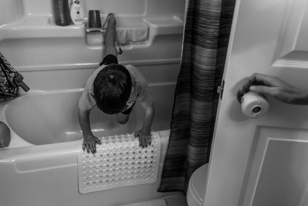 boy hooks toes into shower rail while balancing on hands on edge of bathub