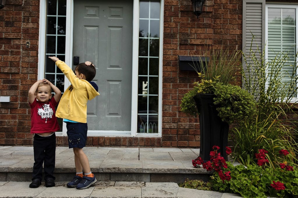 boy in red shirt rests hands on head while boy in yellow shirt measures height difference