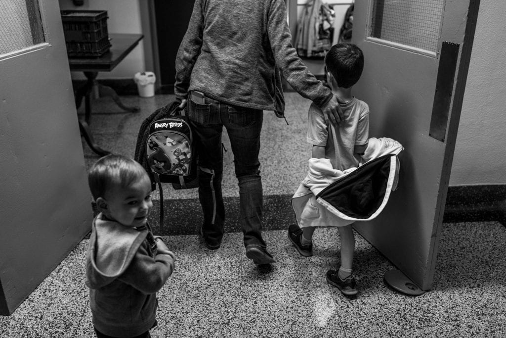 mother reaches hand out to encourage son while brother looks away