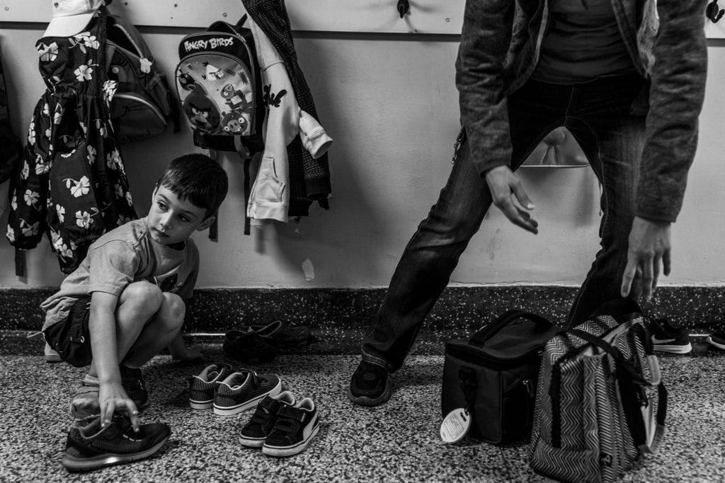 boy looks around while organising shoes and mother reaches for bags