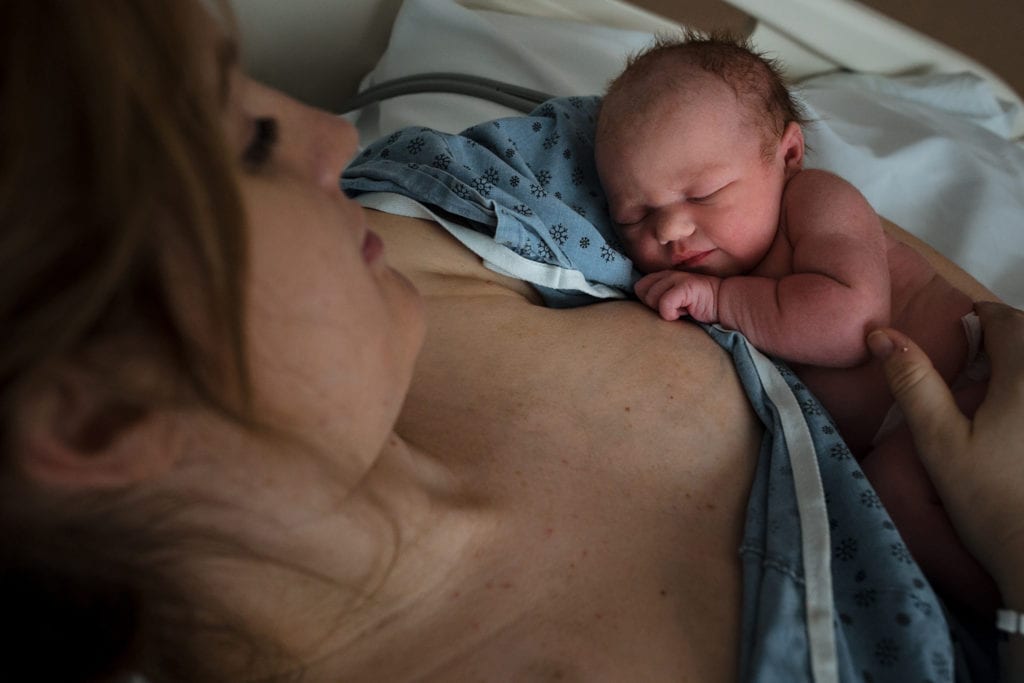 Newborn baby sleeps against mother wearing hospital gown
