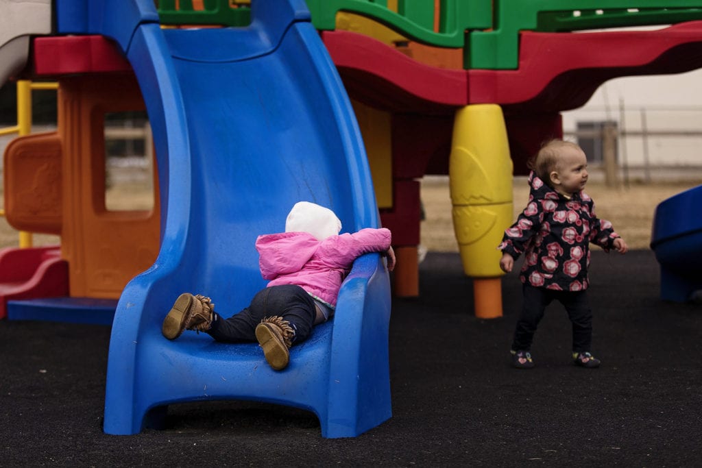 girl lies on bottom of slide while sister walks away