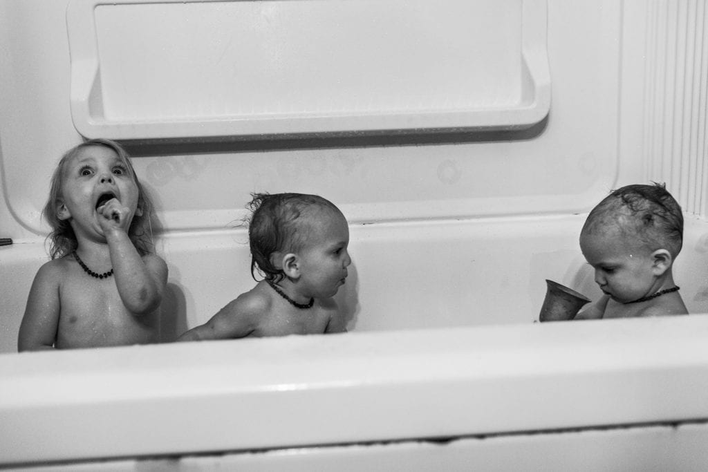 sister makes wild face in bathtub as twins play with toys