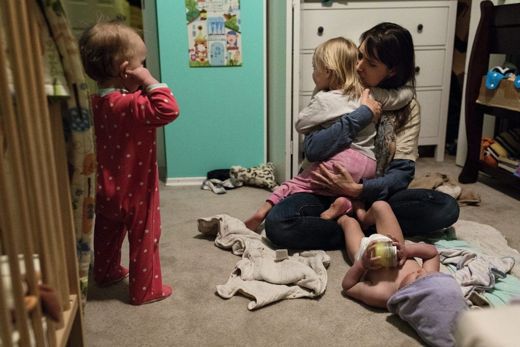 mom hugs daughter amidst towels and pyjamas while prepping three girls for bed