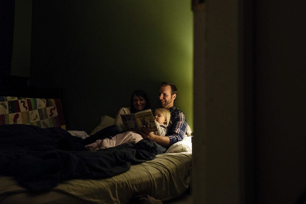 mom and dad lie on bed with daughter reading a book