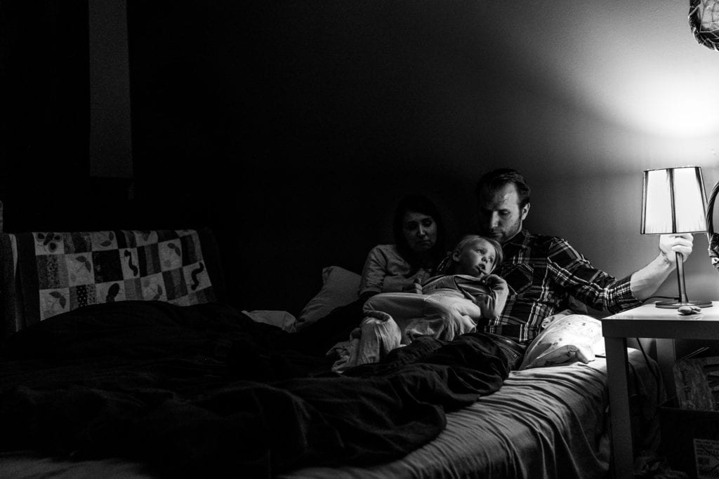 parents lie on bed with daughter who looks towards lamp as dad pulls switch