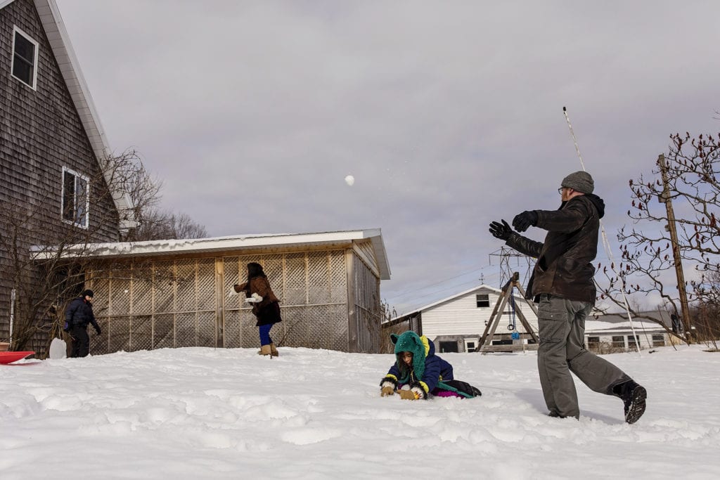 Family having snowball fight in front of wooden shed