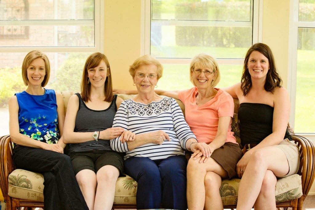 5 women sit side by side on couch in summer attire