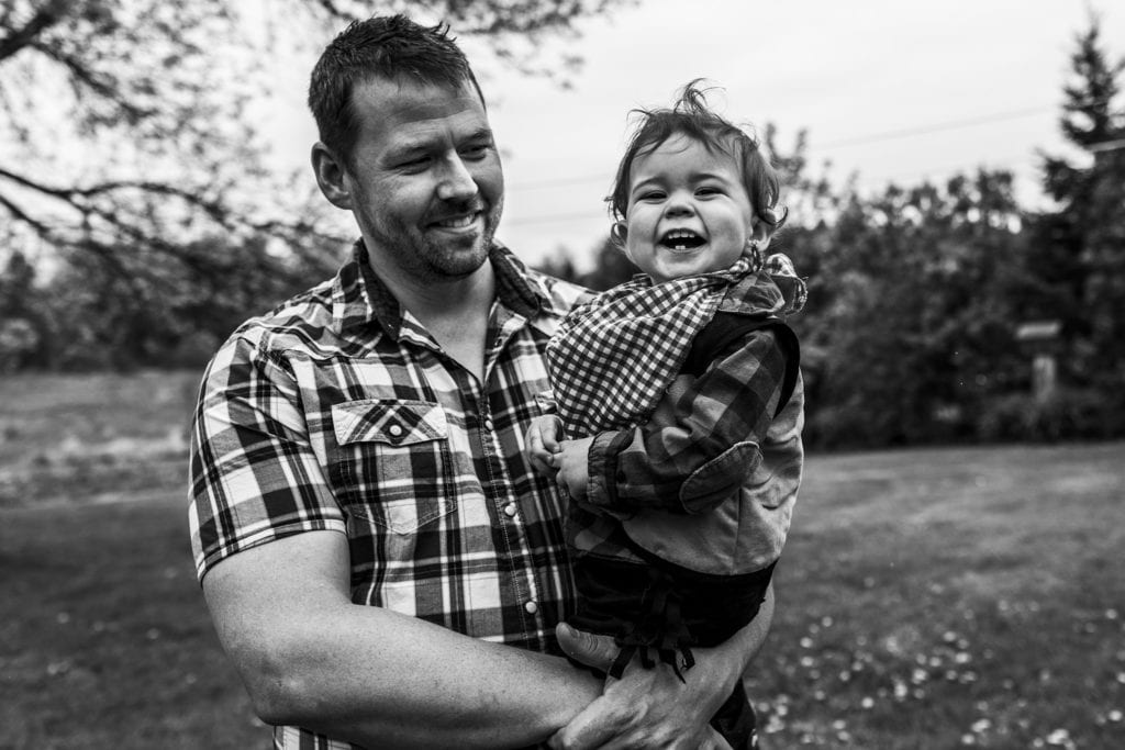 boy in checked shirt smiles widely while dad holds him