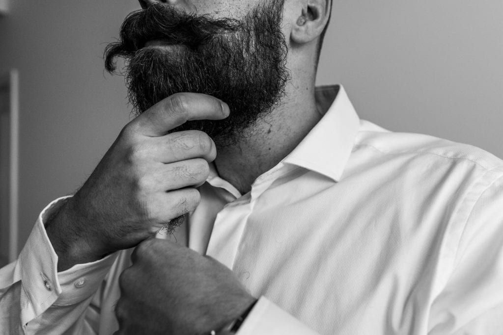 groom hand strokes his beard to smooth it after twirling moustache ends