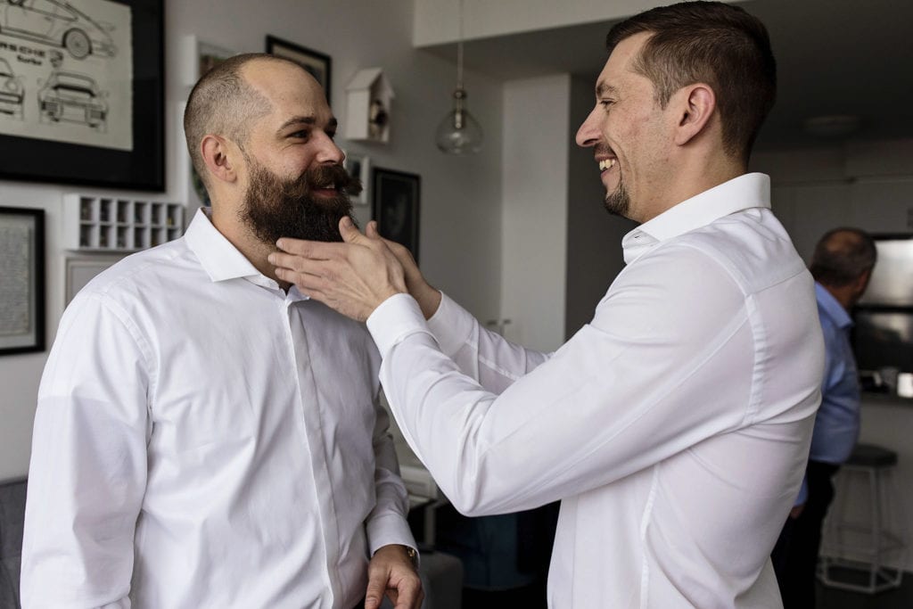 groomsman smoothes groom's luxurious beard as they prepare for wedding day